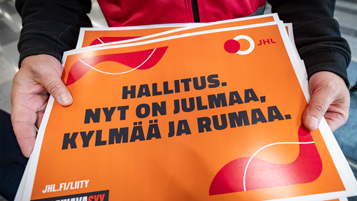 Ihminen pitää JHL-lakkokylttiä kädessään lentoasemalla.