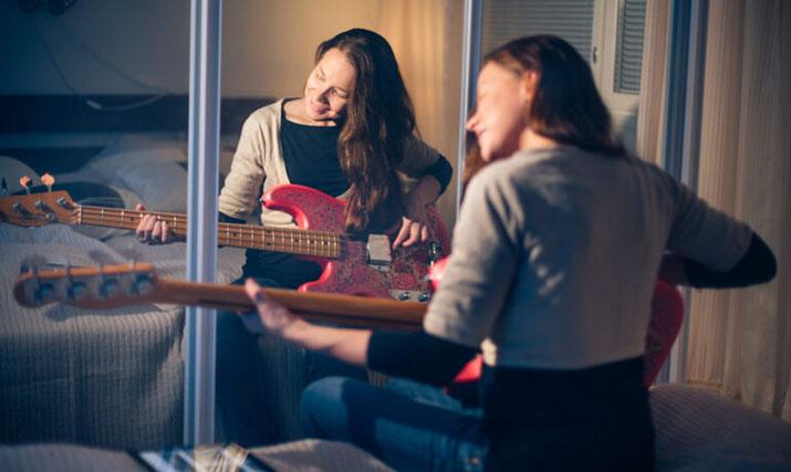 Nuori nainen soittaa kitaraa. JHL:n jäsenenä voit opetella soittamaan todella edulliseen hintaan. Jäsenyys kannattaa.