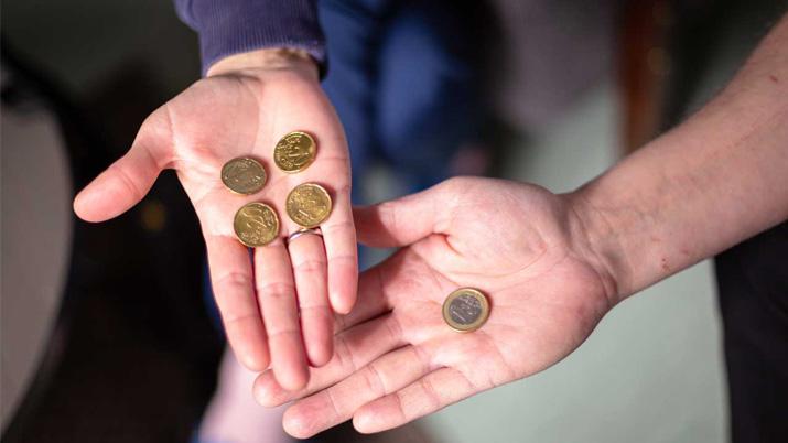 Toisessa käsessä neljä kolikkoa, toisessa yksi euro