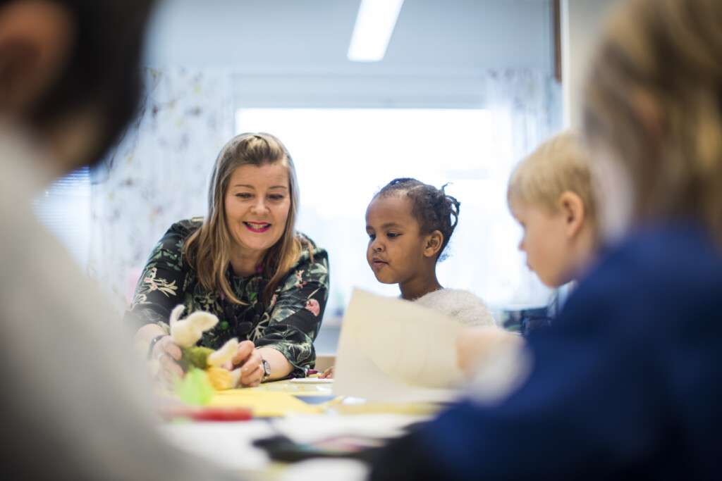 Lapset askartelevat päiväkodissa lastenhoitajan kanssa.