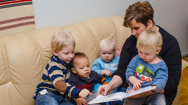 Perhepäivähoitaja lukee kirjaa neljälle hoitolapselle