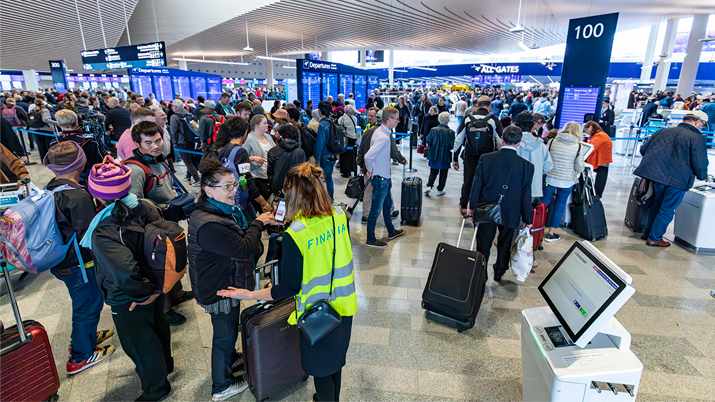Paljon ihmisiä odottamassa pääsyä lentokentän turvatarkastukseen, valoisa lentokenttärakennus.