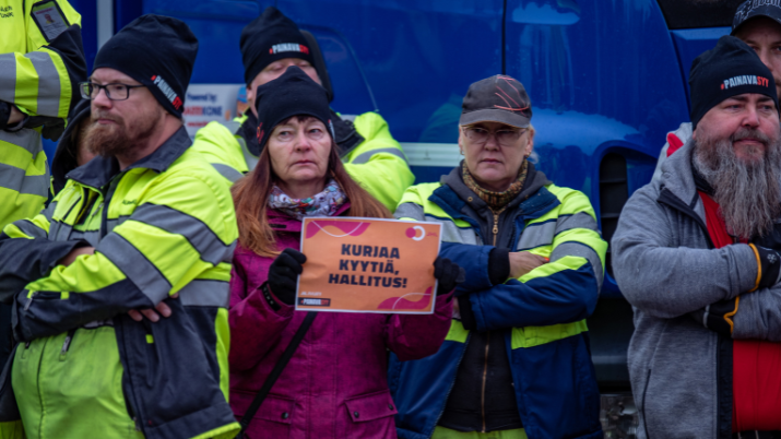 Painava syy -mielenilmaus. Riihimäen teknisen toimen työntekijät keskeyttivät työnteon ja ajoivat ajoneuvoja Riihimäen vanhalle torille. Työntekijän kädessä on kyltti, jossa lukee "kurjaa kyytiä hallitus".