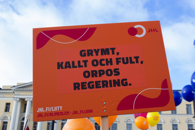 JHL:s orangea skylt med texten "Grymt, kallt och fult, Orpos regering".