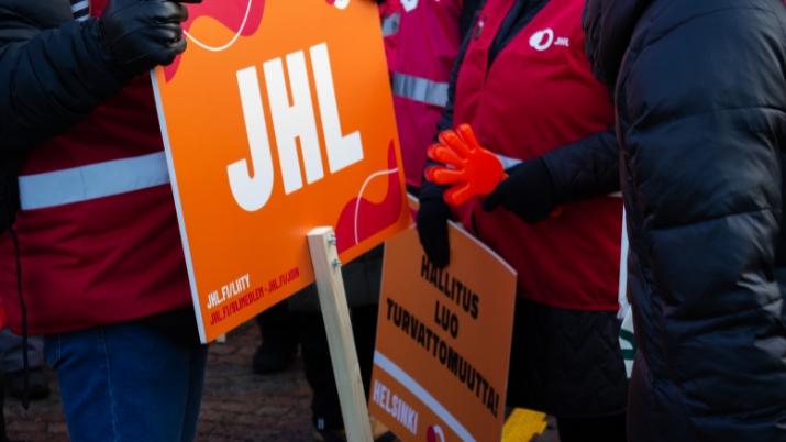 JHL:n kylttejä ja lakkoliivejä Stop nyt -mielenosoituksessa ihmisjoukossa. Painava syy.