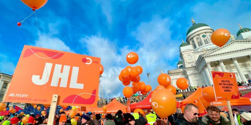 JHL:n lakkokyltti ja paljon ihmisiä Helsingin Senaatintorilla, taustalla Tuomiokirkko. Aurinkoinen päivä, taivaalla vaaleita pilviä.