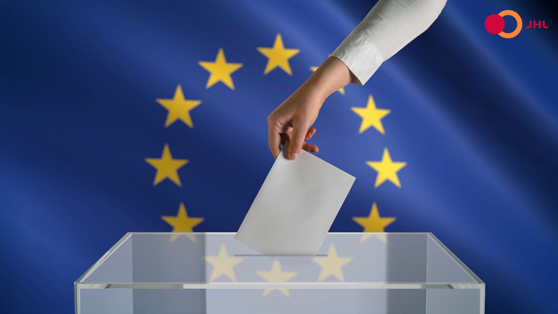 Euroopan Unionin lipun edessä on vaaliuurna, johon käsi vie äänestyslipukkeen.