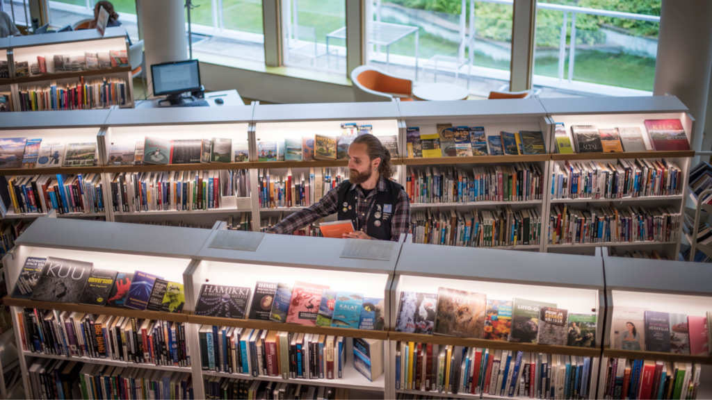 En vy snett ovanifrån av en person som står mellan två fulla bibliotekshyllor.