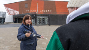Marianne From seisoo pihalla asiakkaan kanssa. Fromilla on valkoinen keppi kädessä.